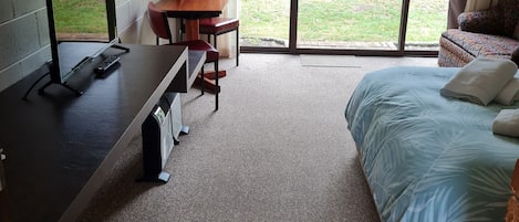 Una habitación con una cama, un escritorio con una computadora, una silla y vistas al exterior por una puerta corredera.