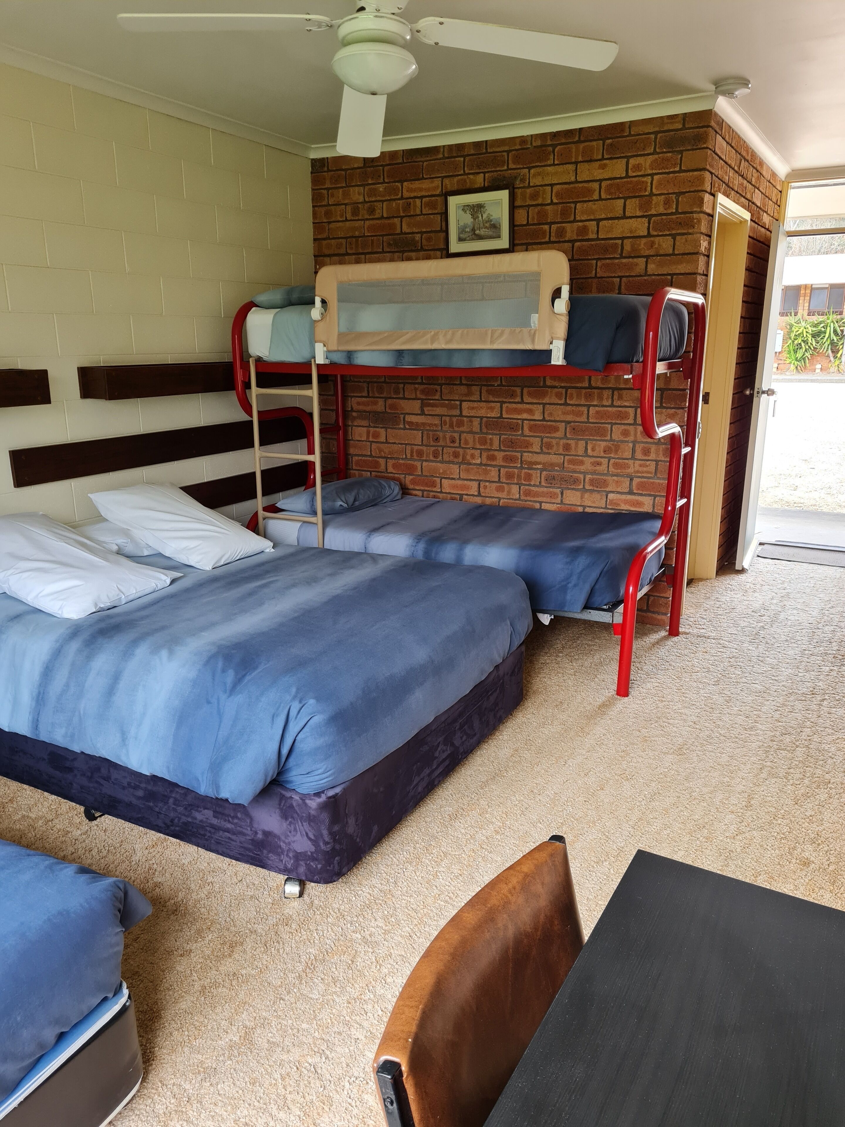 A bunk bed room with a brick wall, a ceiling fan, and a door leading outside.