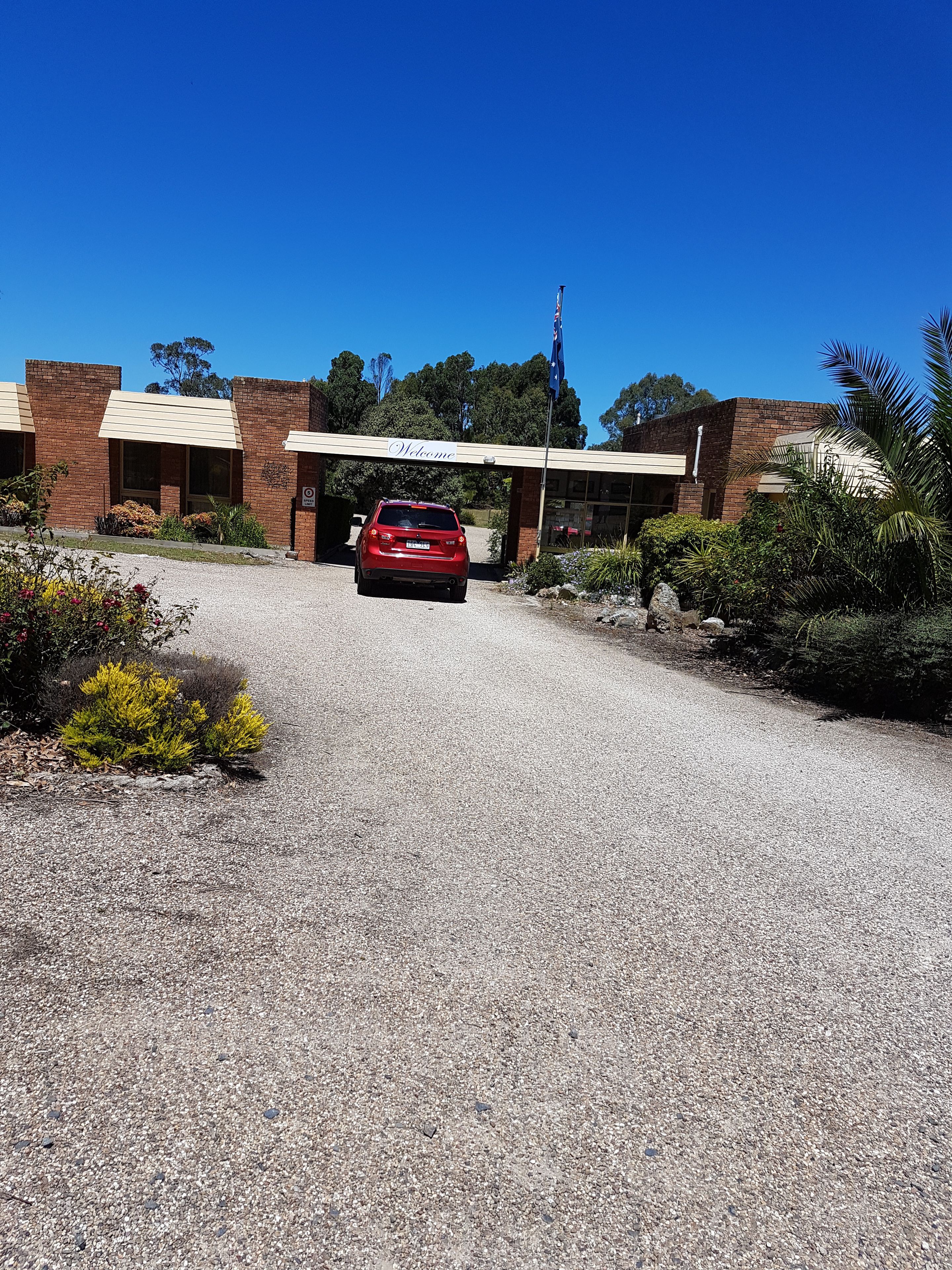 A building with a 'Welcome' sign, a red car parked in front, and a flagpole with a flag.