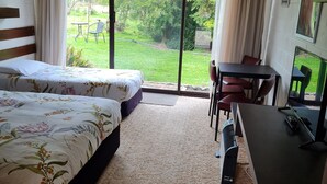 Habitación de hotel con dos camas, un escritorio, una silla, un televisor y vista a un jardín.