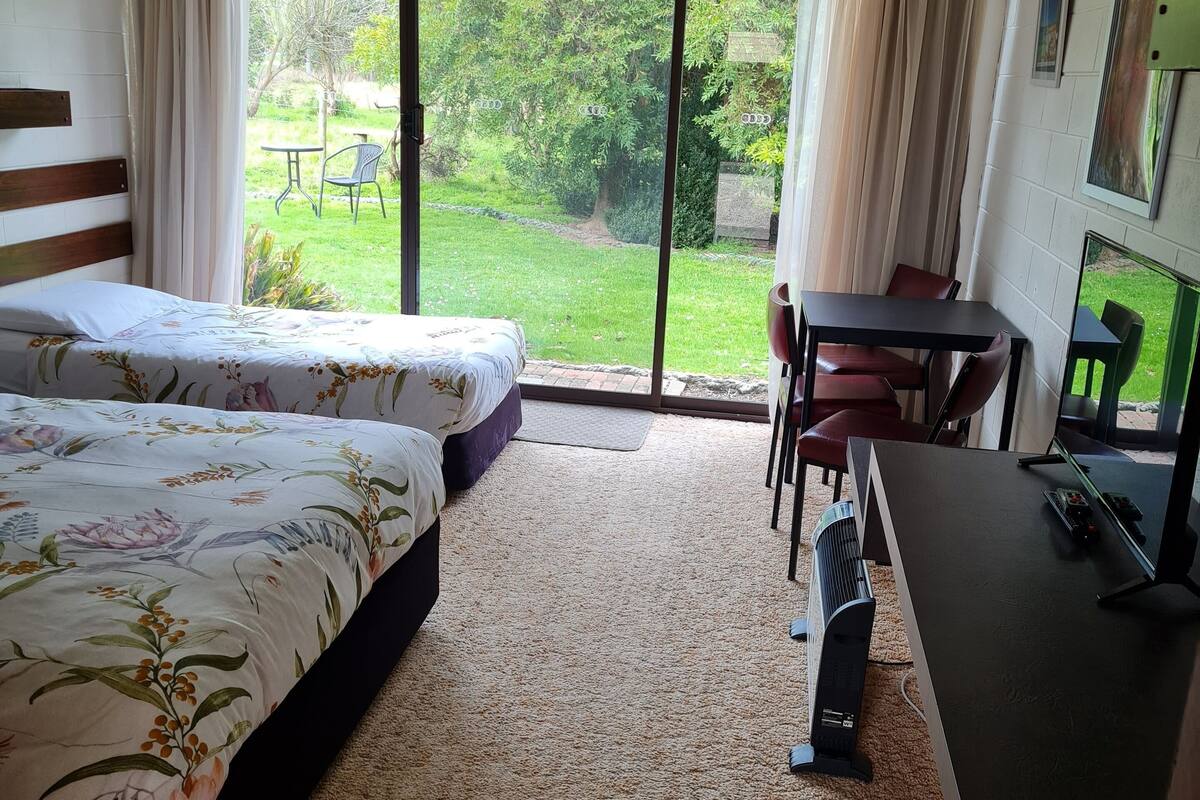 Habitación de hotel con dos camas, un escritorio, una silla, un televisor y vista a un jardín.