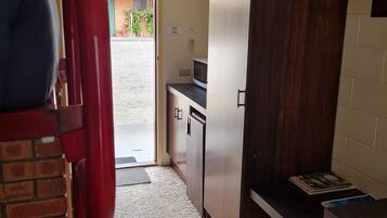 A compact kitchen with a microwave, a small refrigerator, and a wooden cabinet.