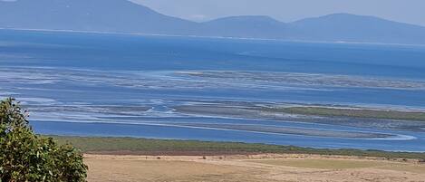 A coastal landscape with rolling hills, a clear sky, and a distant mountain range.
