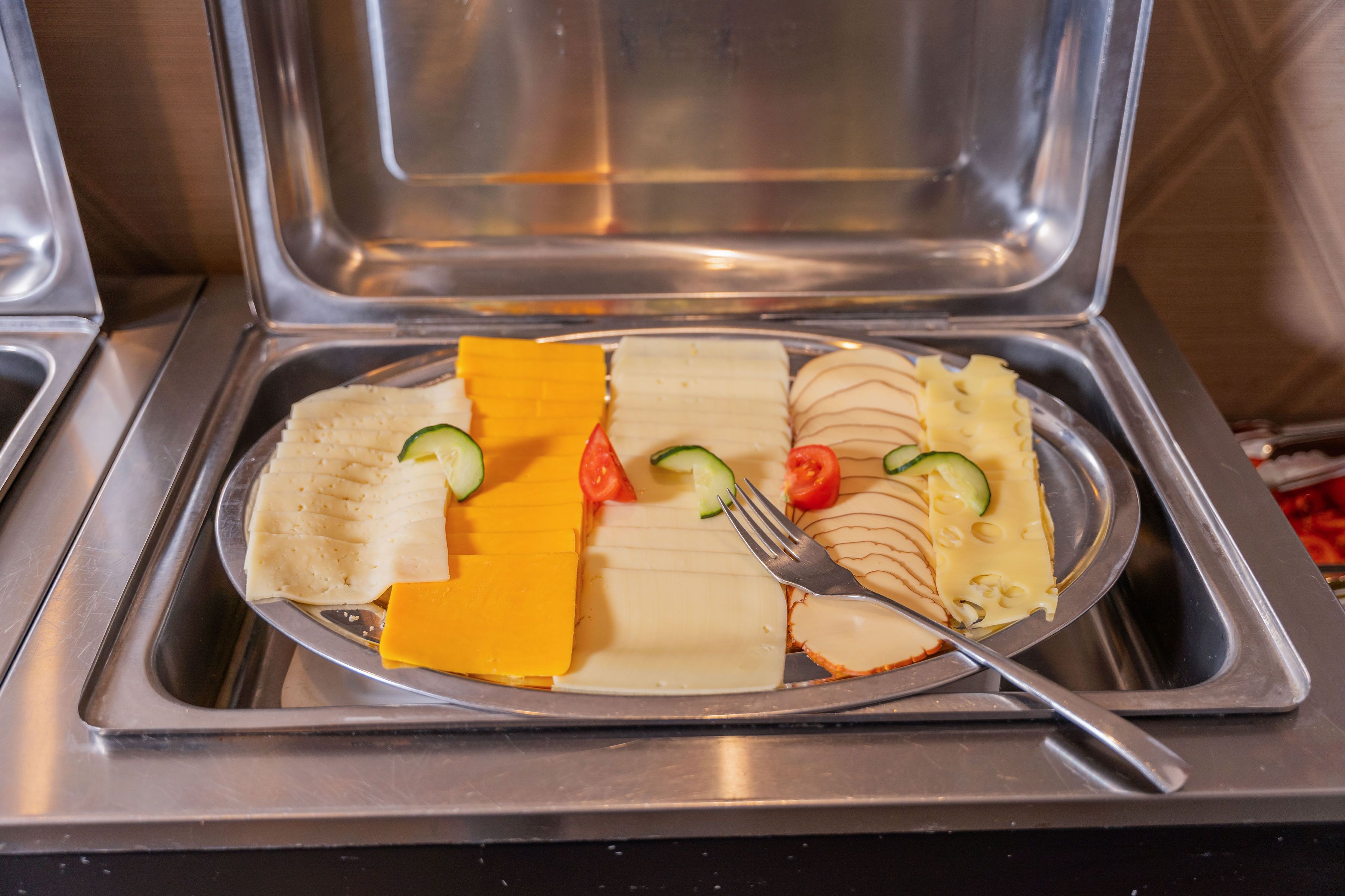 Un bufé con distintos alimentos, entre ellos queso, pepinos y tomates.