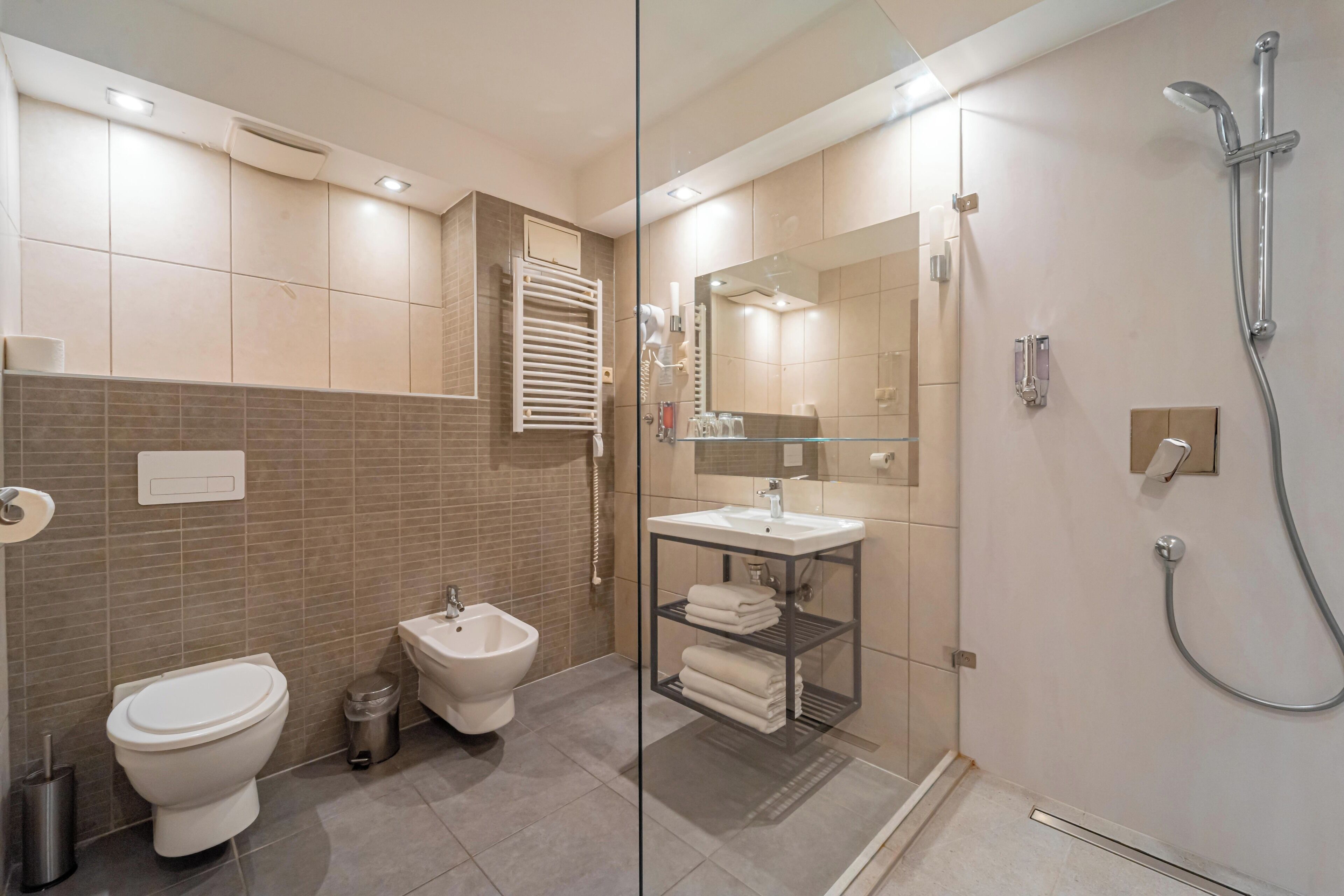 A modern bathroom with a glass shower enclosure, a bidet, a toilet, and a vanity with a mirror.