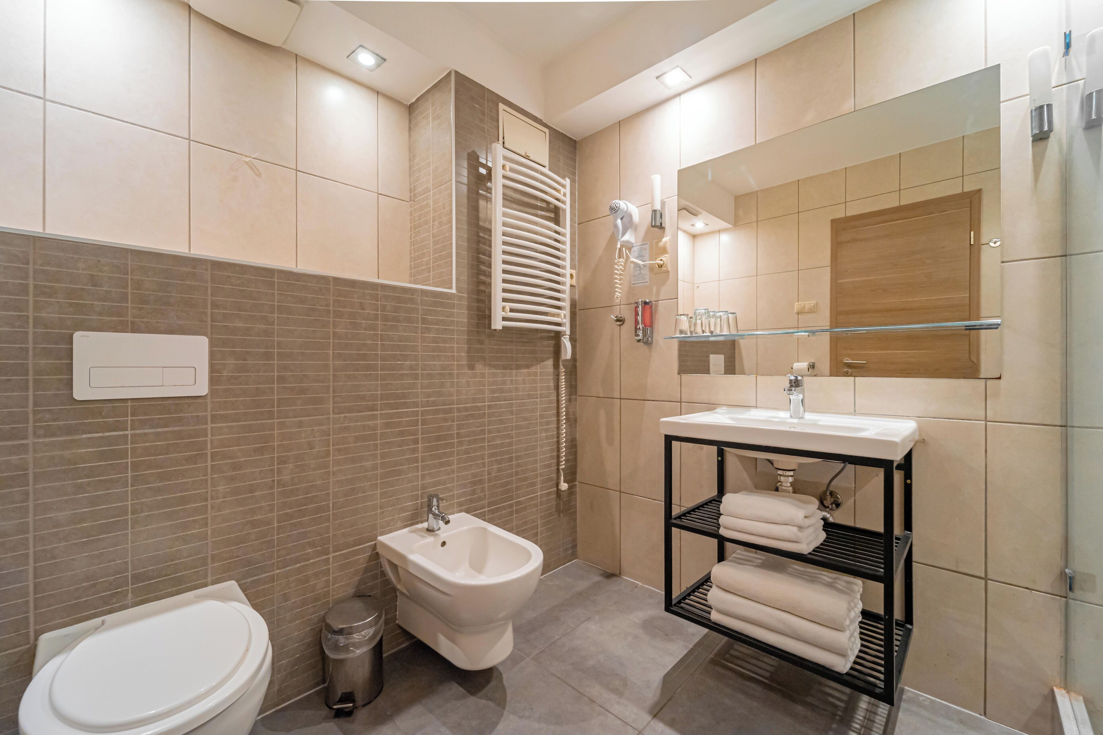 Uma casa de banho moderna com bidé, sanita, lavatório e porta-toalhas.