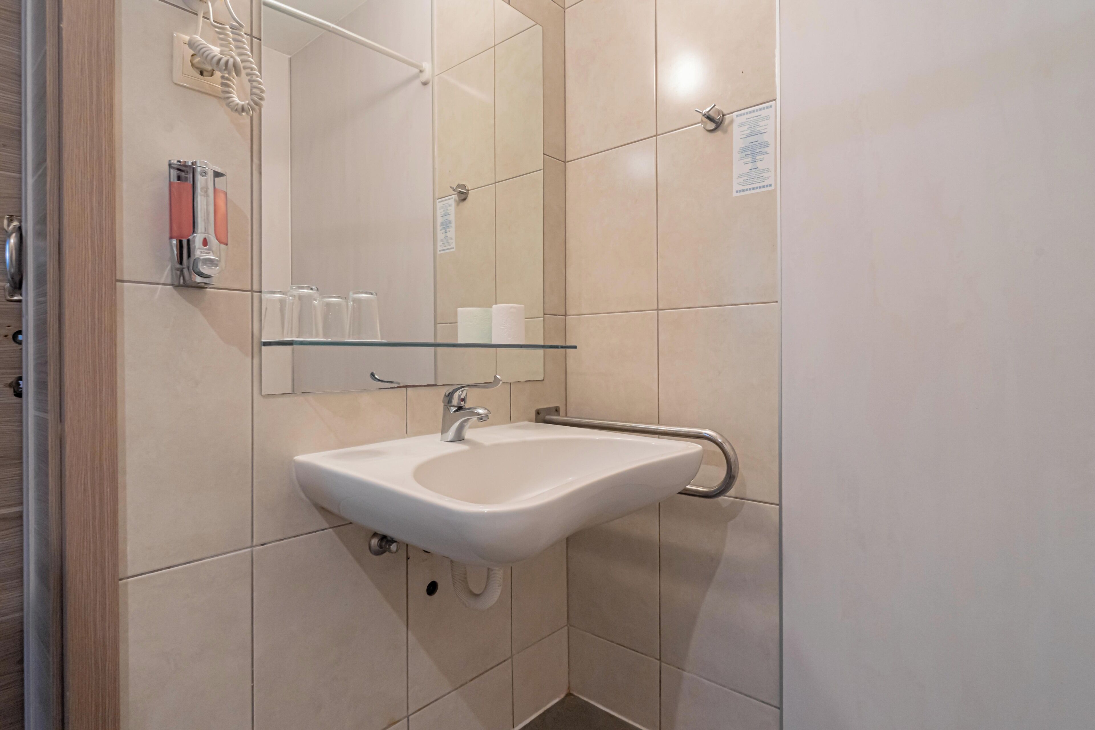 A bathroom with a white sink, a mirror, and a glass shelf.