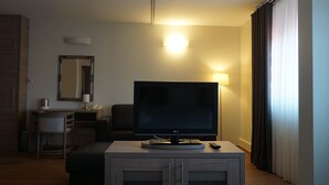 Ein Hotelzimmer mit Flachbildfernseher auf einem Holzbock, einem Schreibtisch mit Lampe, einem Spiegel und einem Kleiderschrank.