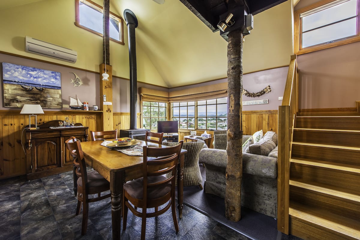 A cozy room with a wooden dining table, chairs, a sofa, and a staircase.