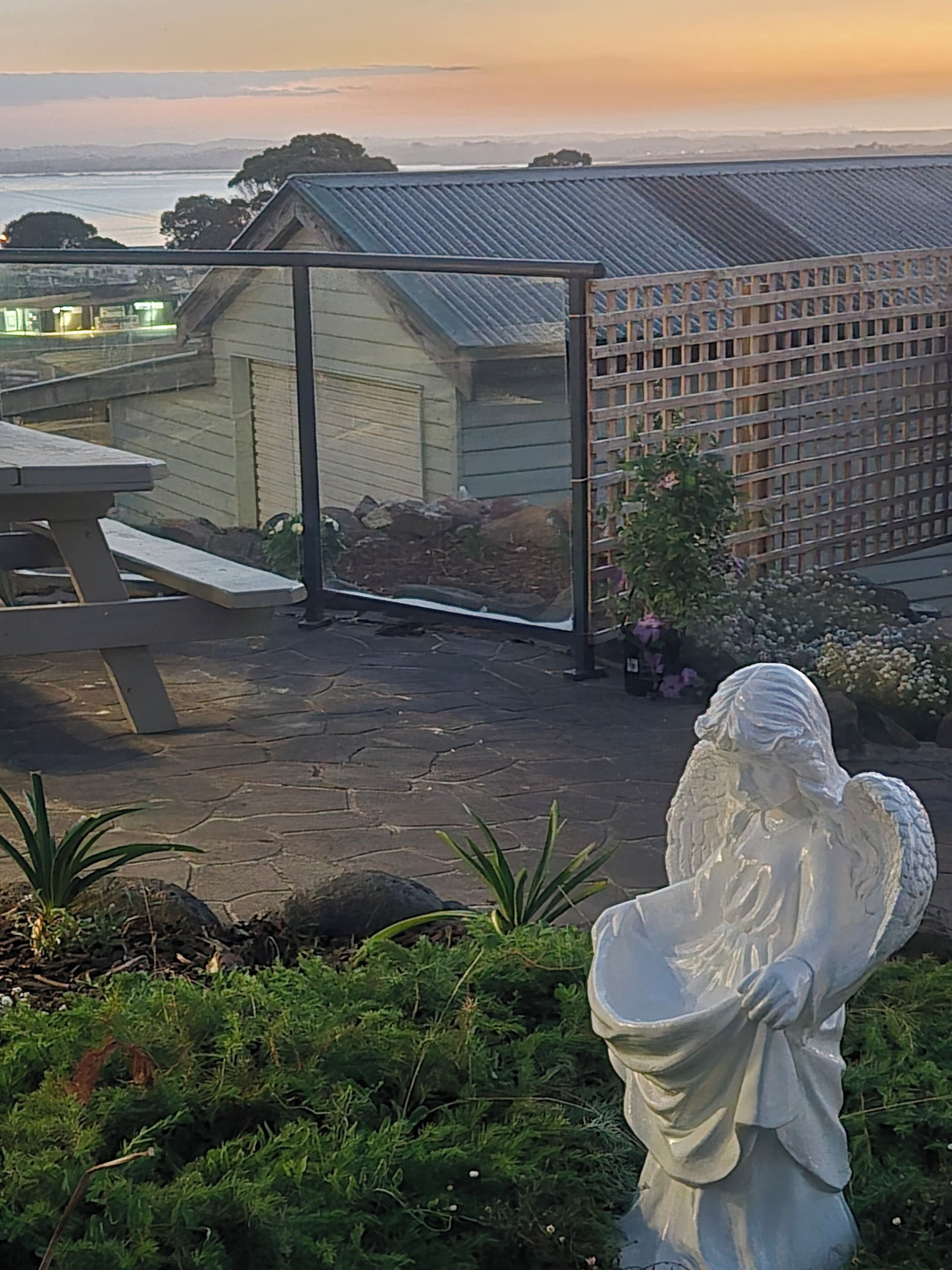 A statue of an angel in a garden setting with a view of a building and a body of water in the background.