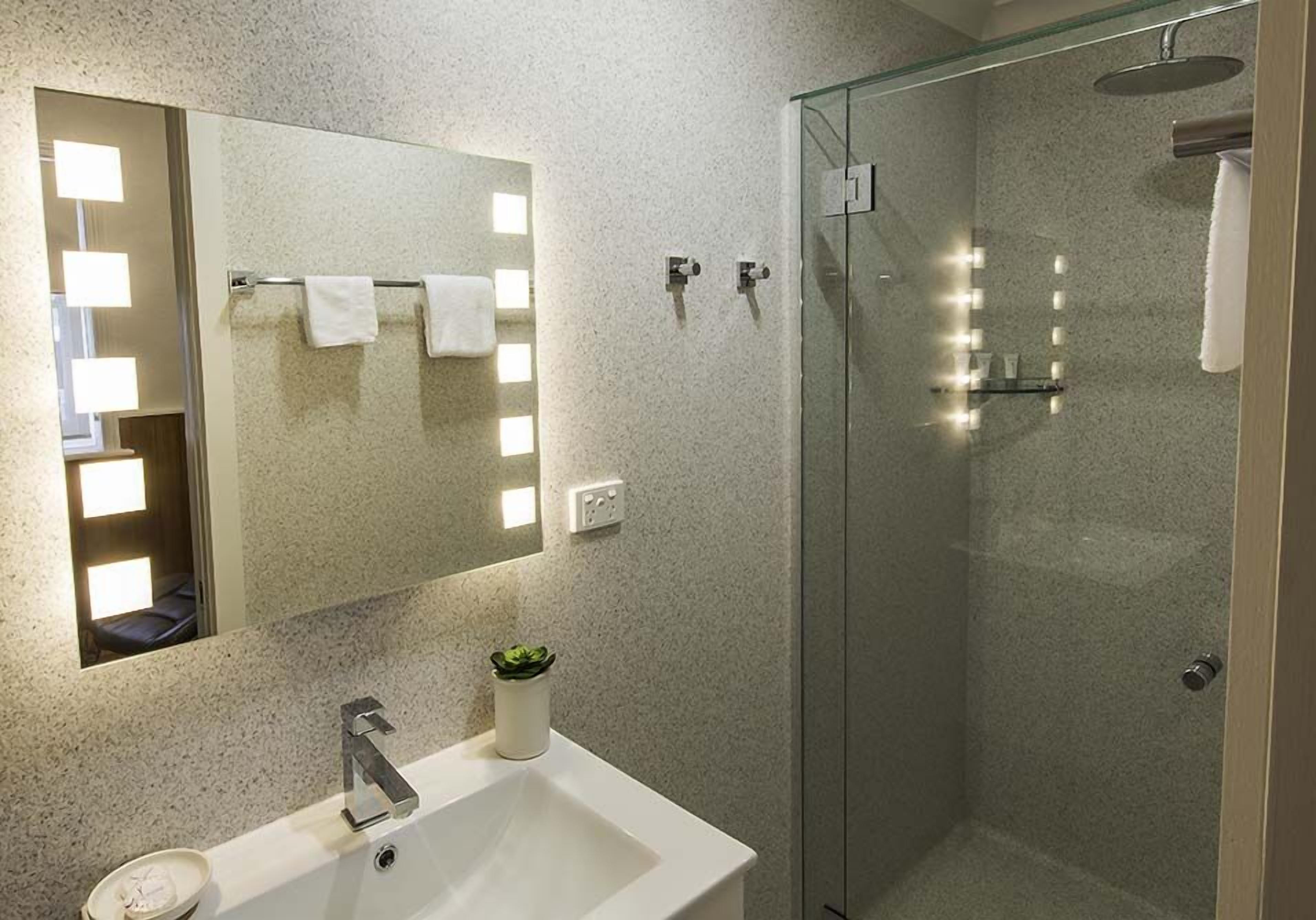 Une salle de bain moderne avec un grand miroir, un lavabo et une douche à parois de verre.