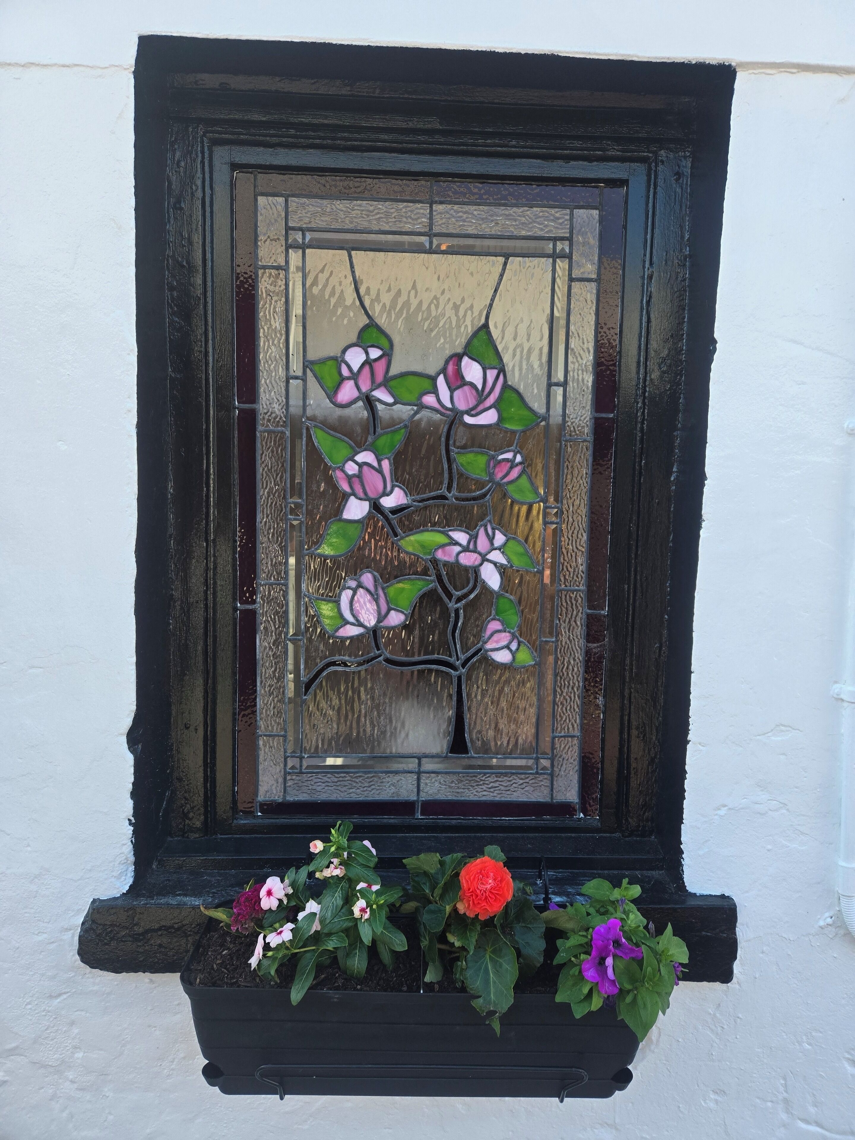 Een glas-in-loodraam met bloemmotieven en een bloembak eronder.
