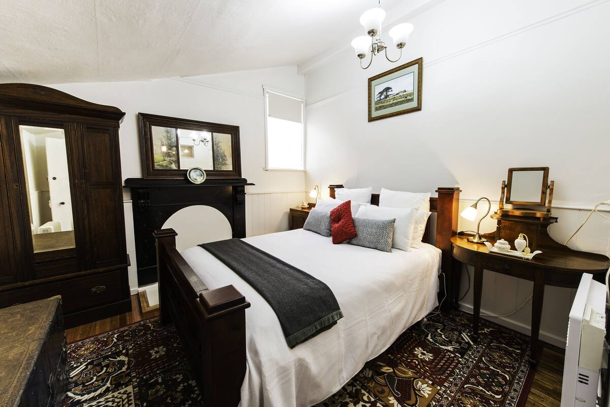 A bedroom with a large bed, a dresser, a desk with a lamp, and a framed picture on the wall.