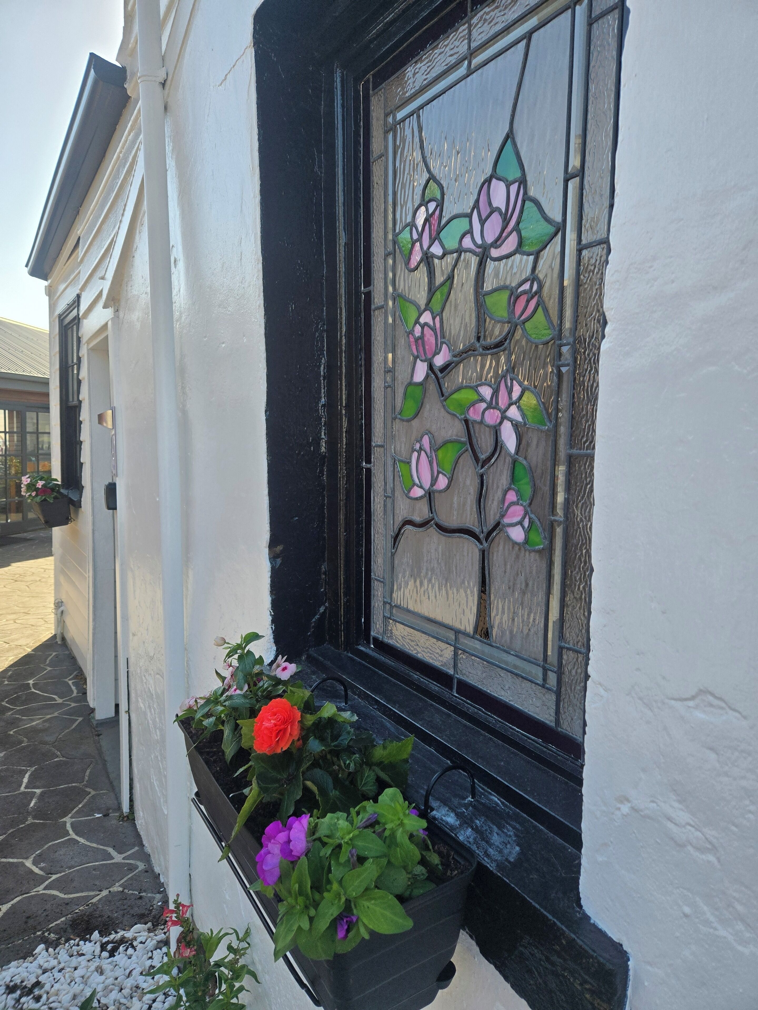 A window with a stained glass design, a black window frame, and a planter with flowers.