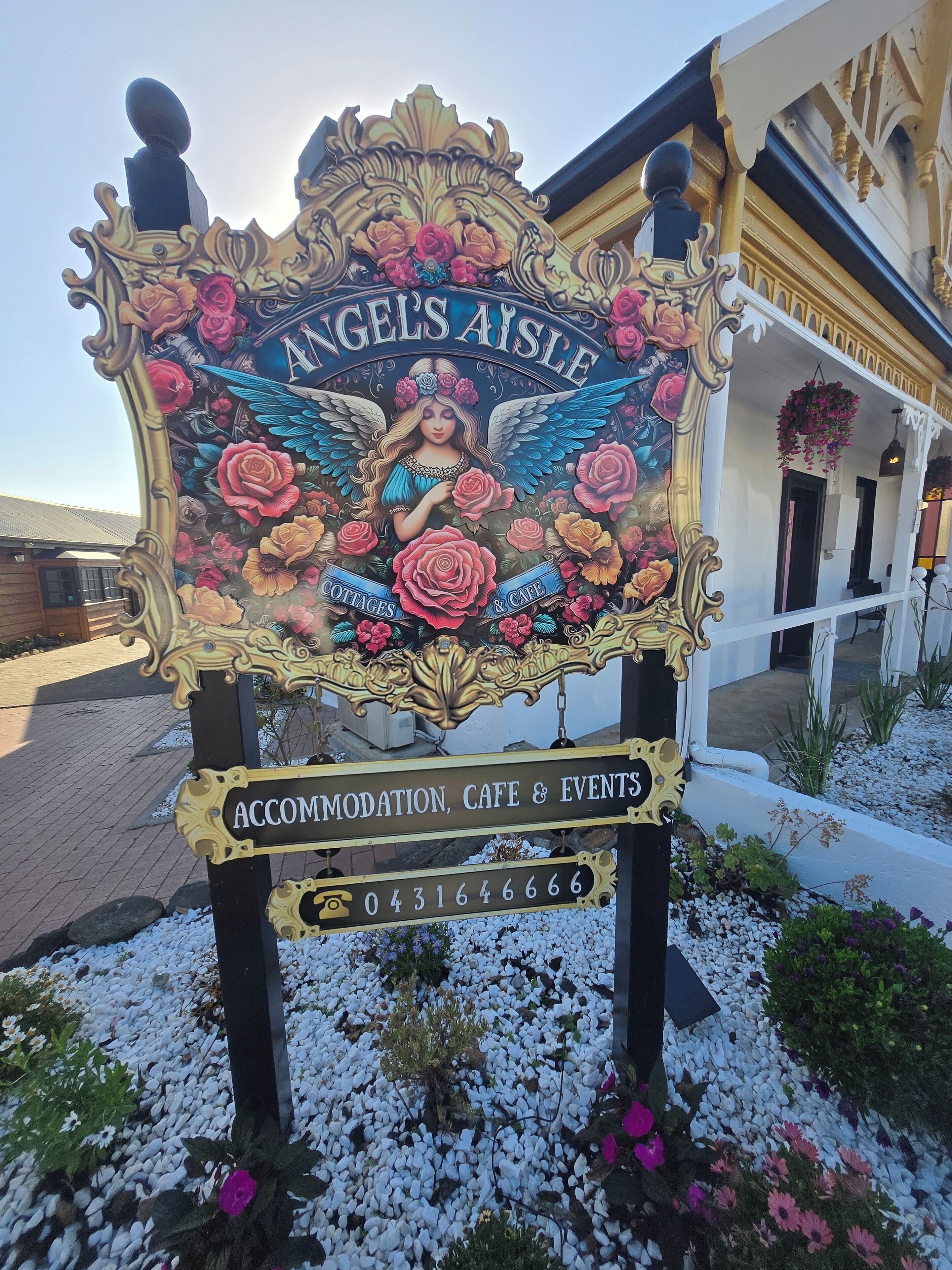 Une enseigne pour « Angels Aisle », avec un motif floral et une illustration d’un ange. Elle fait de la publicité pour l’hébergement, le café et les événements.