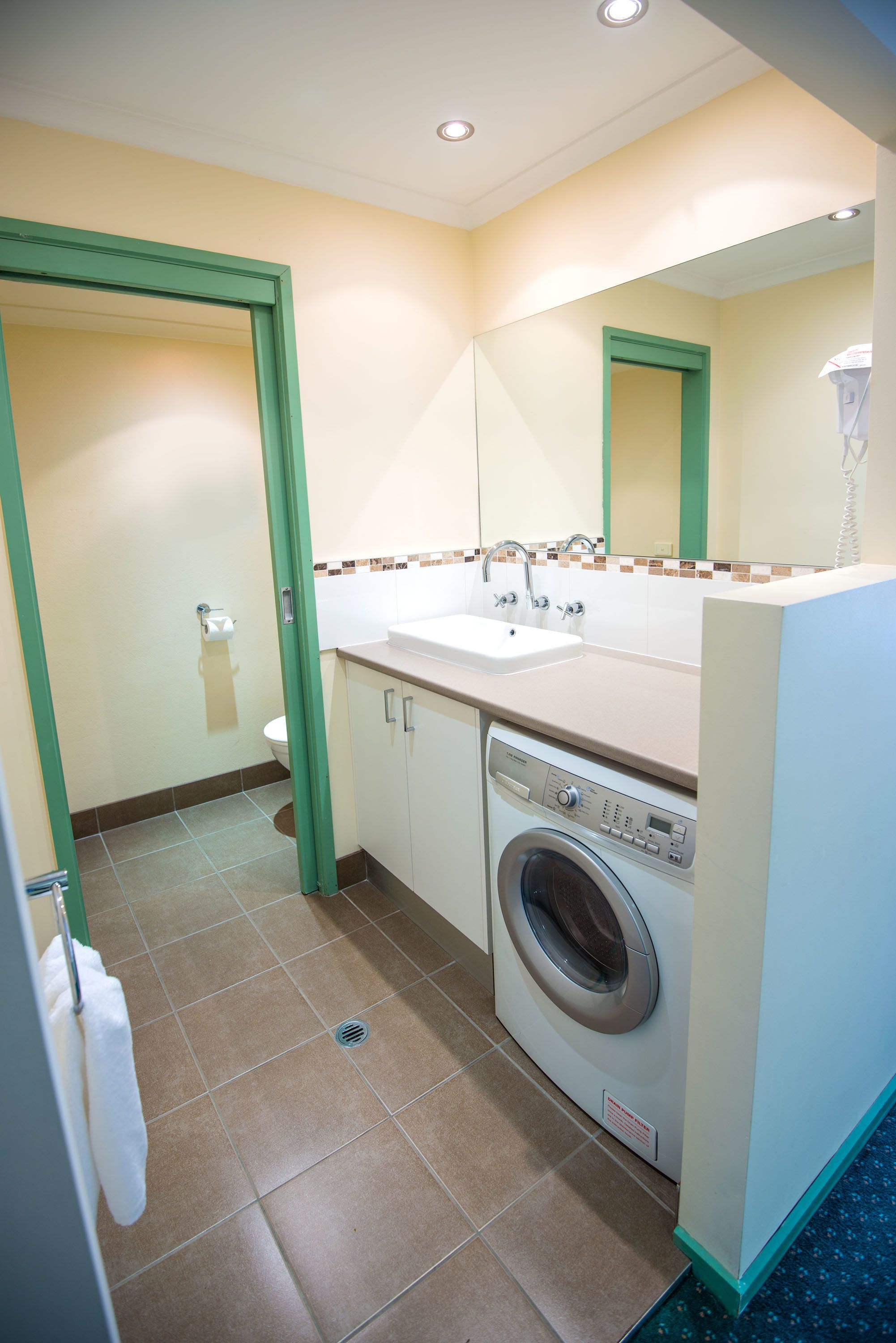 A compact hotel bathroom with a washing machine, sink, and toilet.
