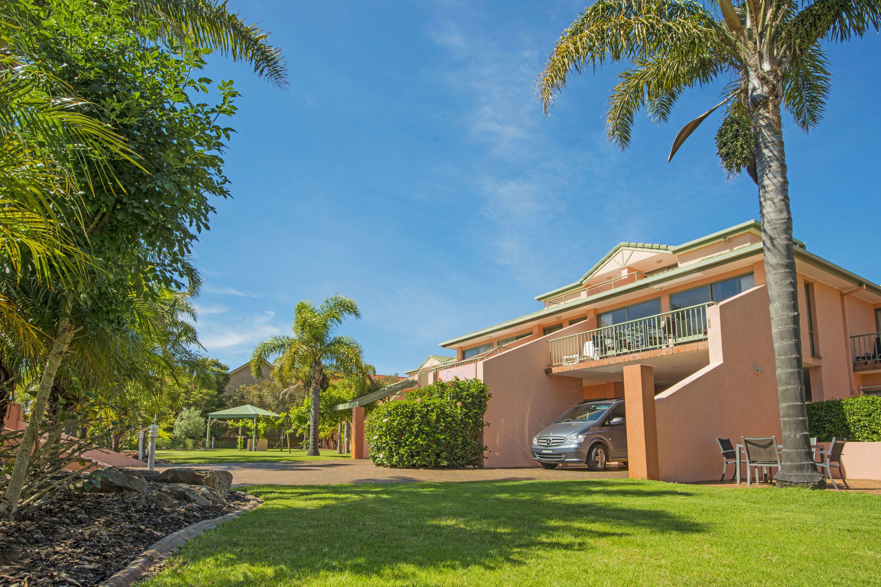 A two-story building with a balcony, surrounded by palm trees and a well-maintained lawn.