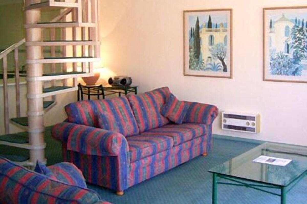 A living room with a striped sofa, a glass coffee table, a staircase, and two framed paintings on the wall.