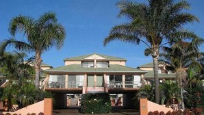 A two-story hotel with a green roof, a covered outdoor area, and palm trees. - Tuscany Apartments (Merimbula)