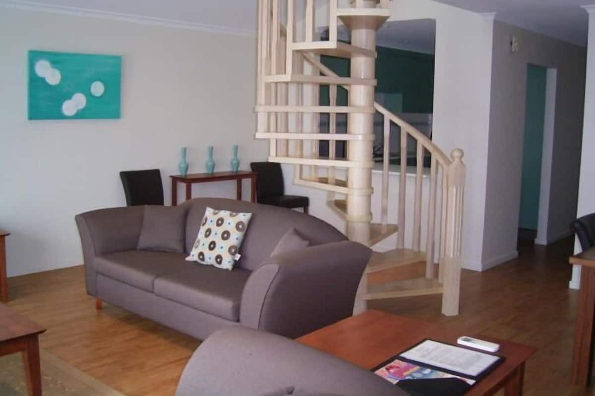 A living room with a grey sofa, a coffee table, and a wooden staircase.