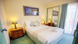 A neatly arranged hotel room with a large bed, two bedside tables with lamps, a mirror, and a framed picture on the wall. - Tuscany Apartments (Merimbula)