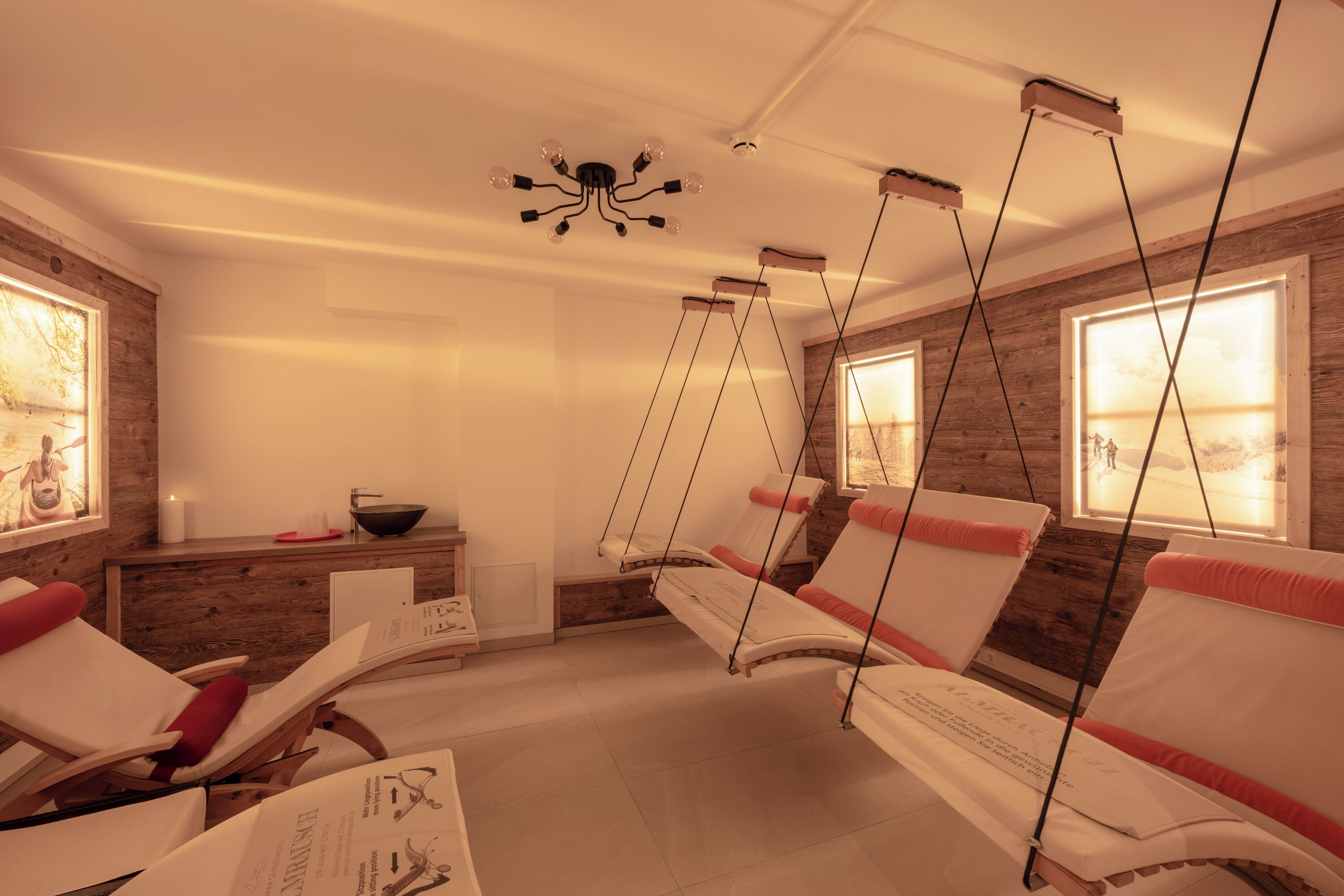 Un cuarto de spa con paredes de madera, una lámpara en el techo y tres sillas reclinables con cojines rojos.