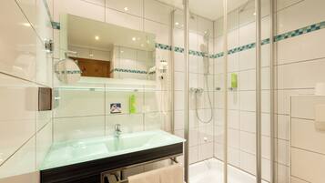 A modern bathroom with a glass sink, a mirror, a glass-enclosed shower, and a towel hanging on a rack.
