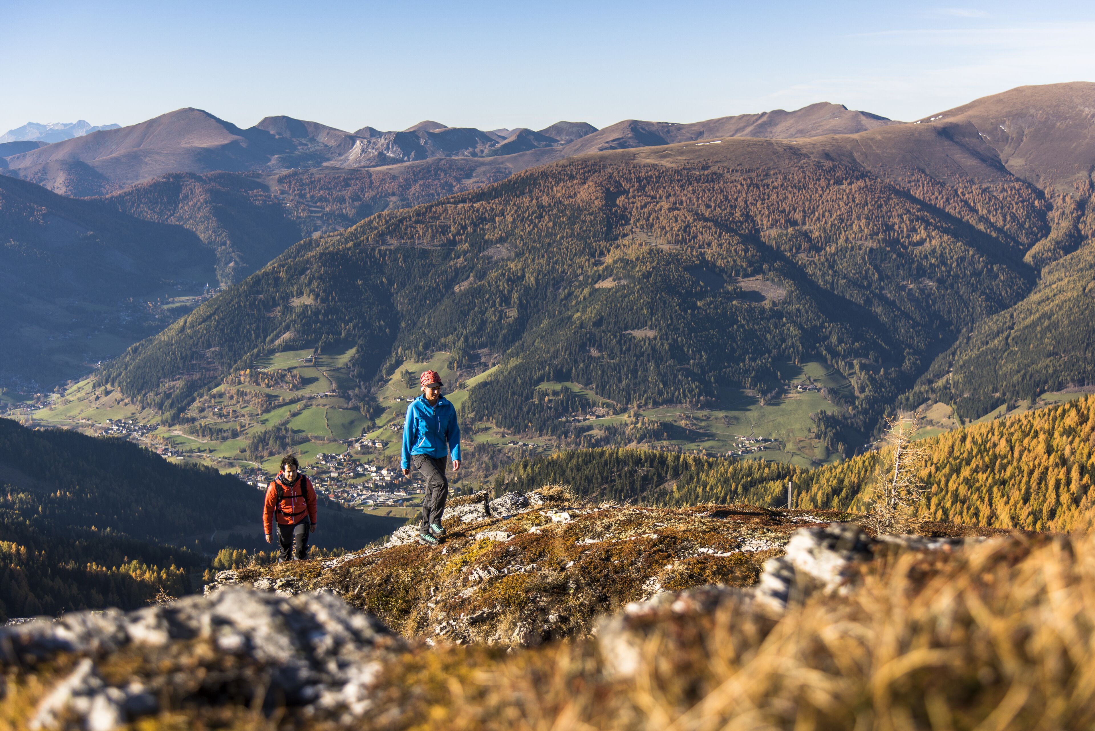 Un paisaje montañoso con una persona con chaqueta azul caminando por un sendero pedregoso.