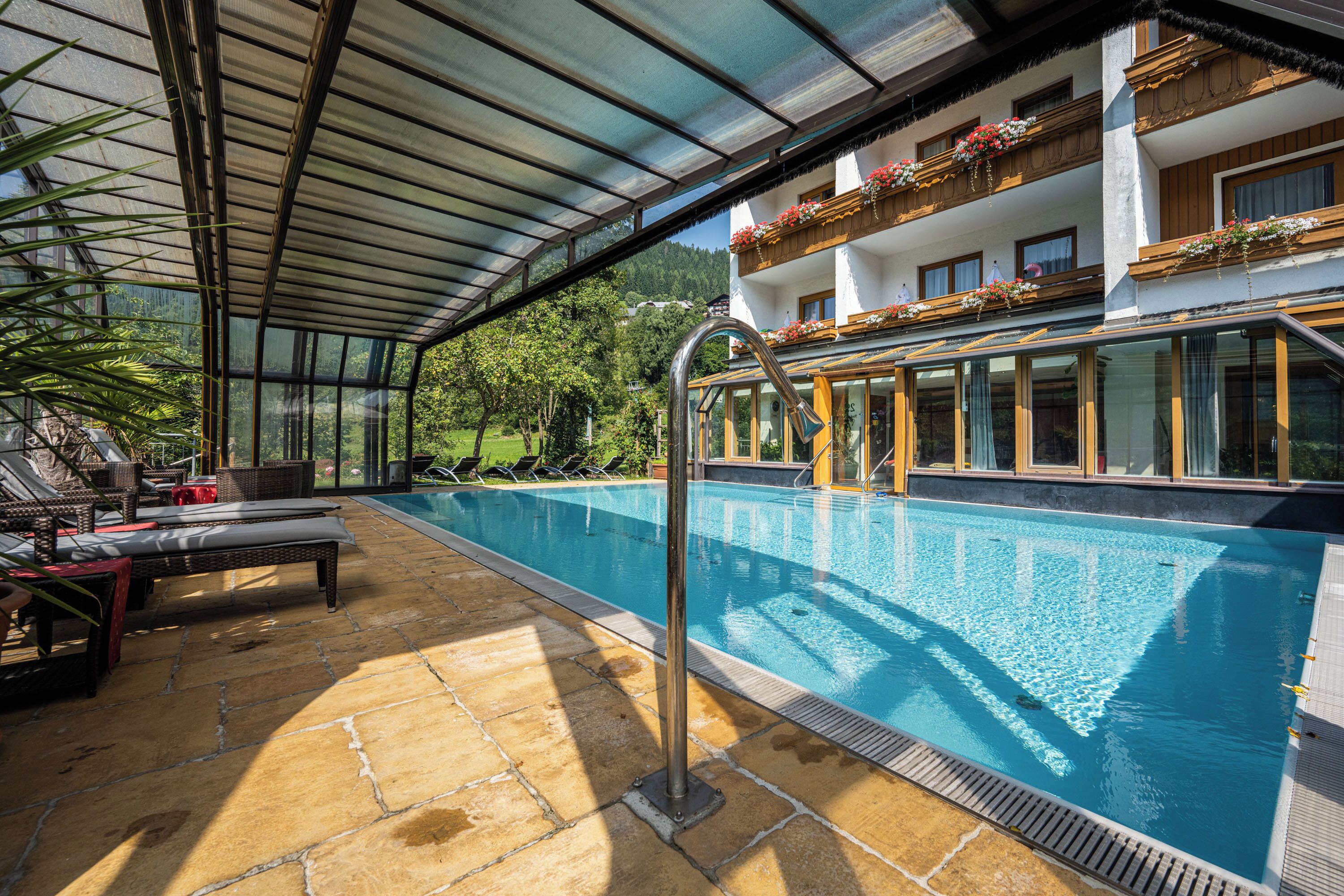 A swimming pool with a glass enclosure, lounge chairs, and a view of a mountain.