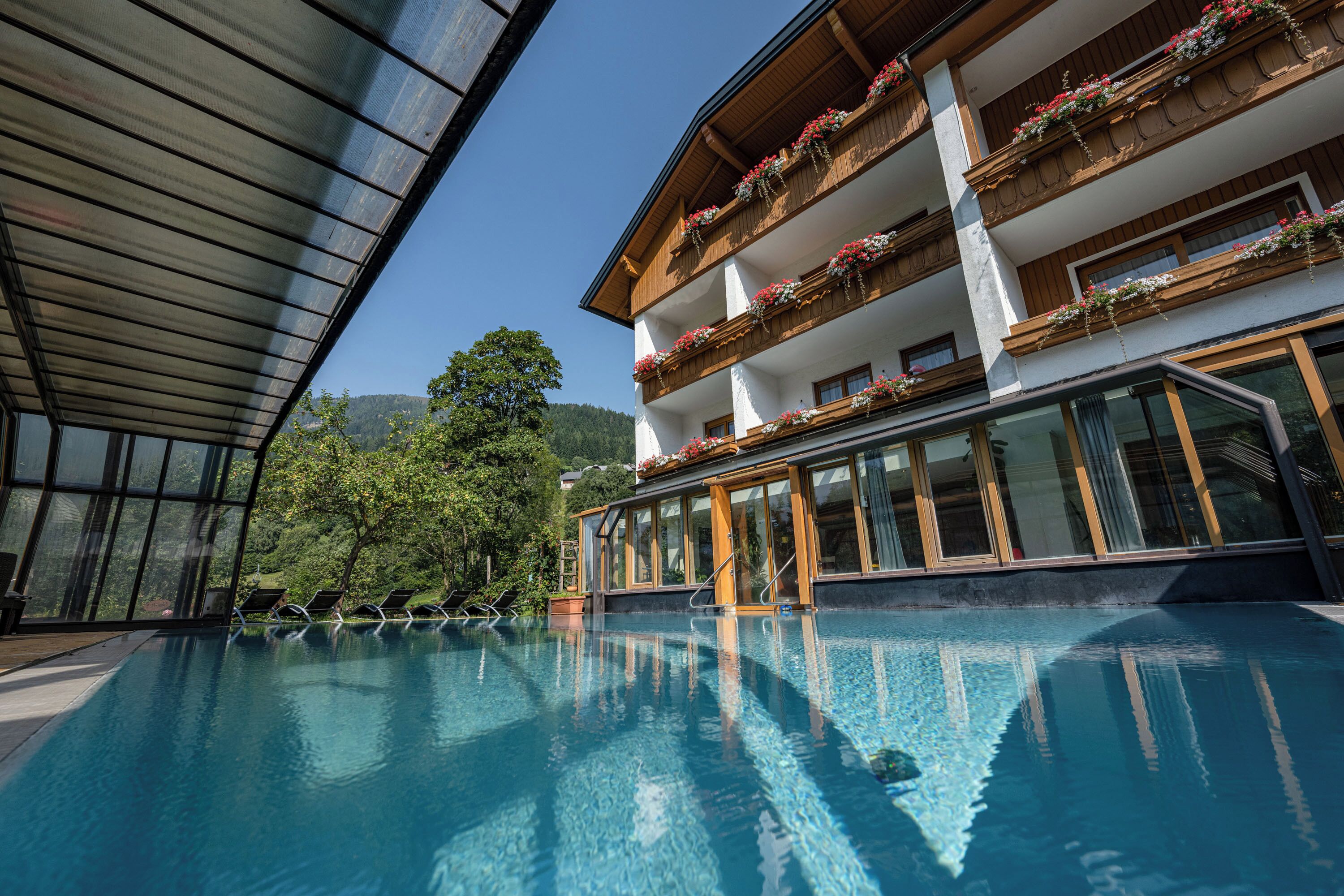 Ein Hotel mit Schwimmbad, Holzbalkonen mit Blumenkästen und großen Fenstern.