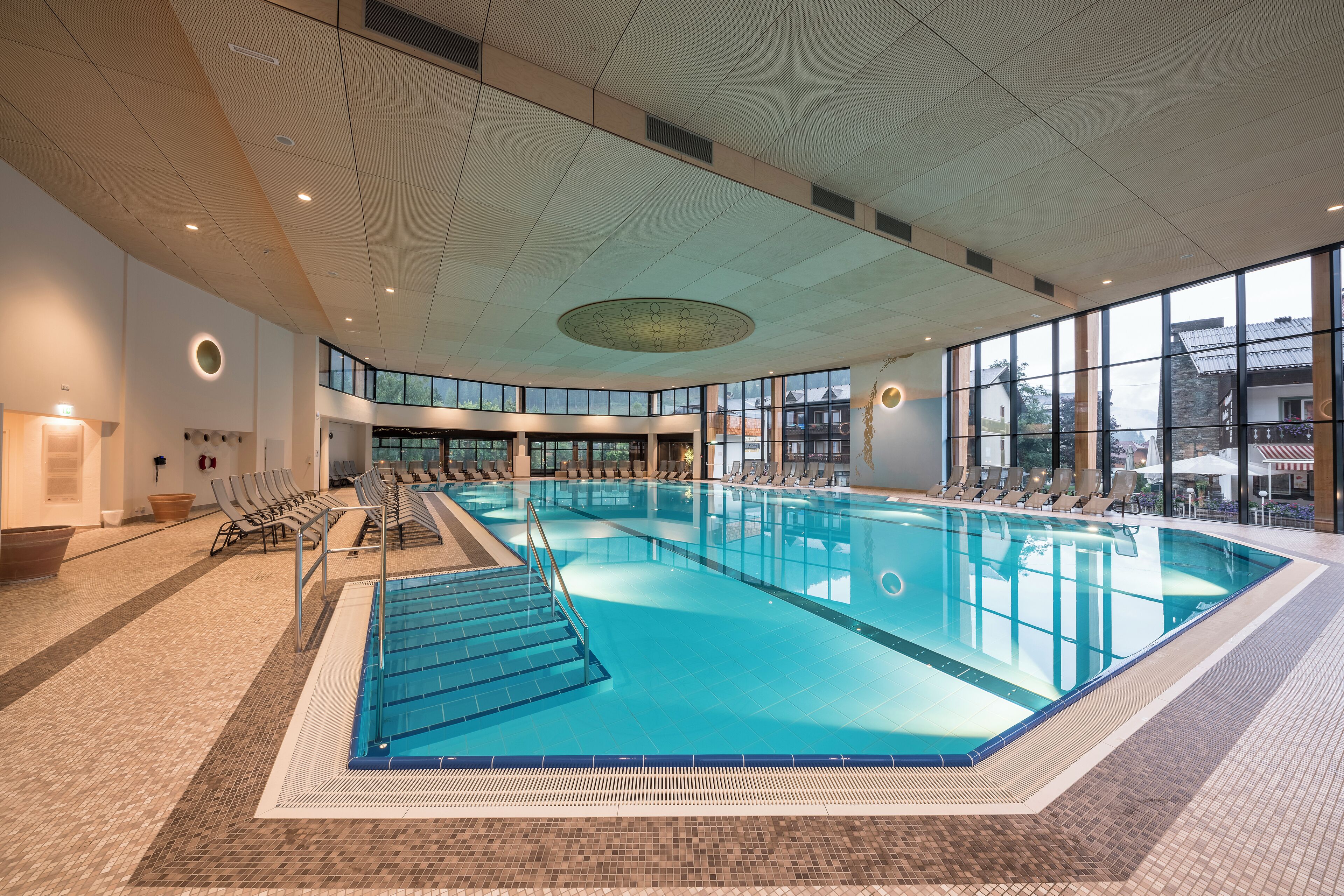 Une piscine intérieure à l’eau claire, entourée de chaises longues et dotée d’un sol carrelé.