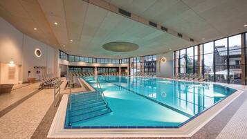 Une piscine intérieure à l’eau claire, entourée de chaises longues et dotée d’un sol carrelé.