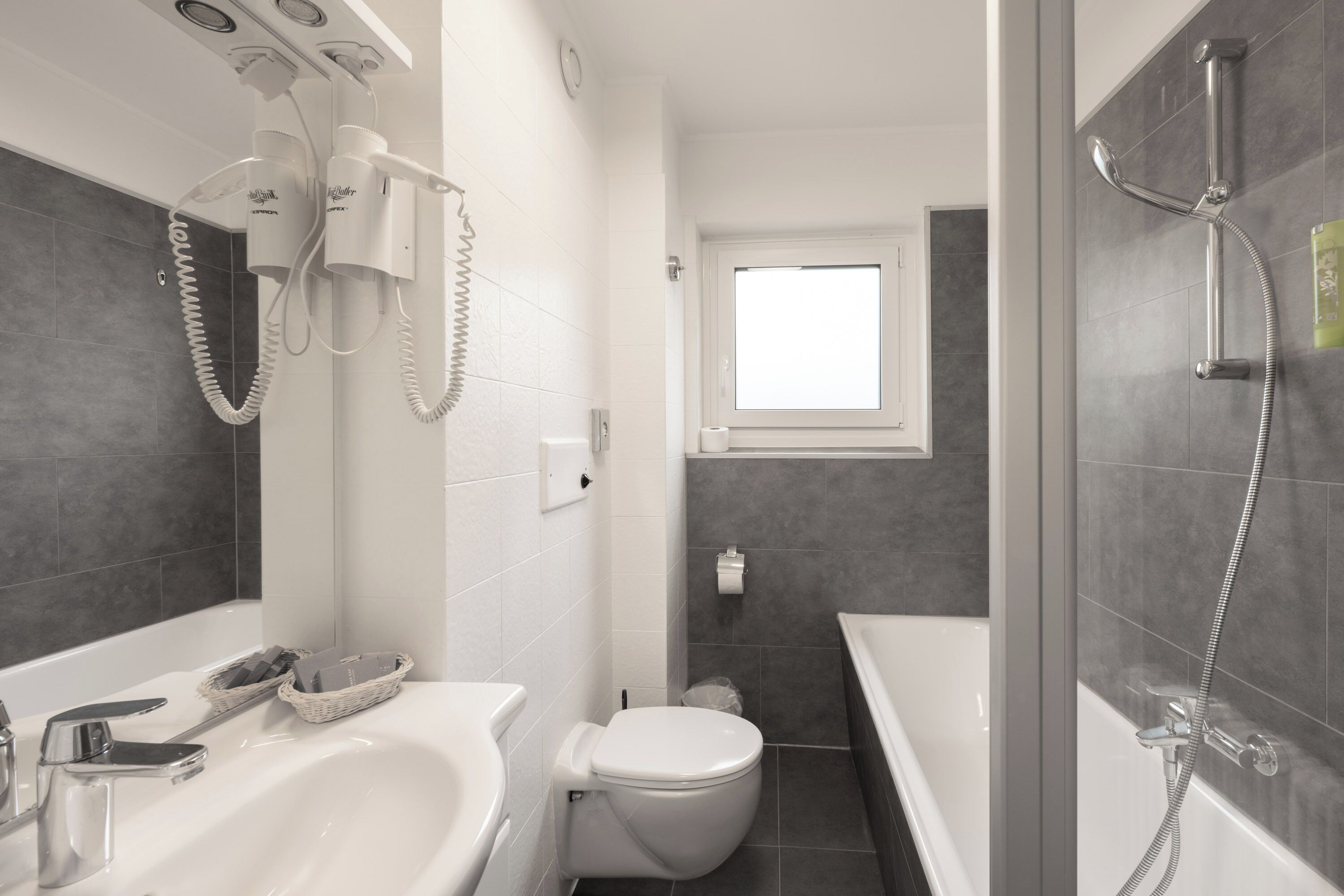 A modern bathroom with a white sink, a toilet, a shower with a handheld showerhead, and a window above the toilet.