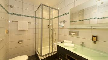 A modern bathroom with a glass-enclosed shower, a white toilet, a glass sink, and a mirror with a decorative tile border.