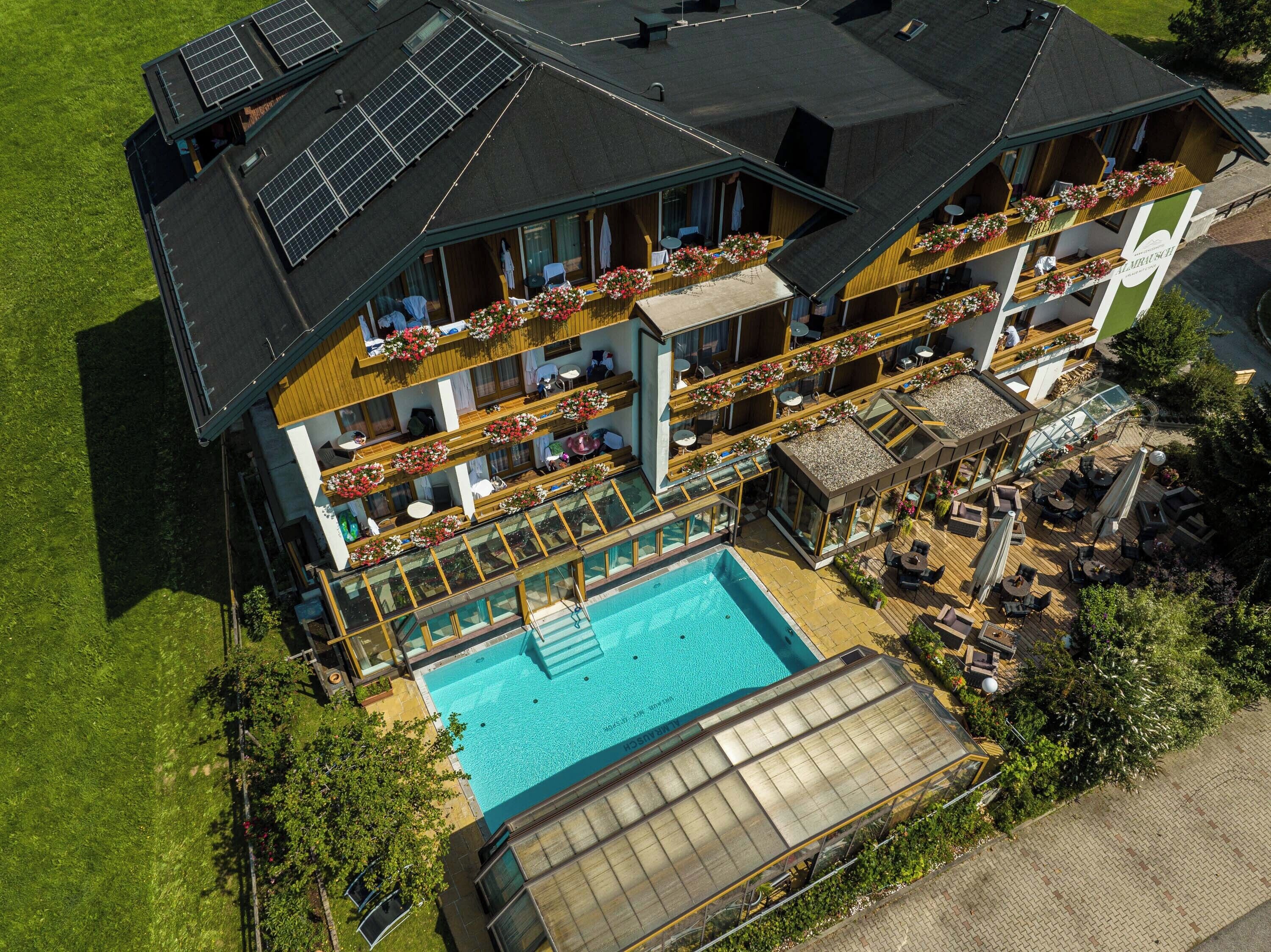 A two-story building with a swimming pool, outdoor seating, and solar panels on the roof.
