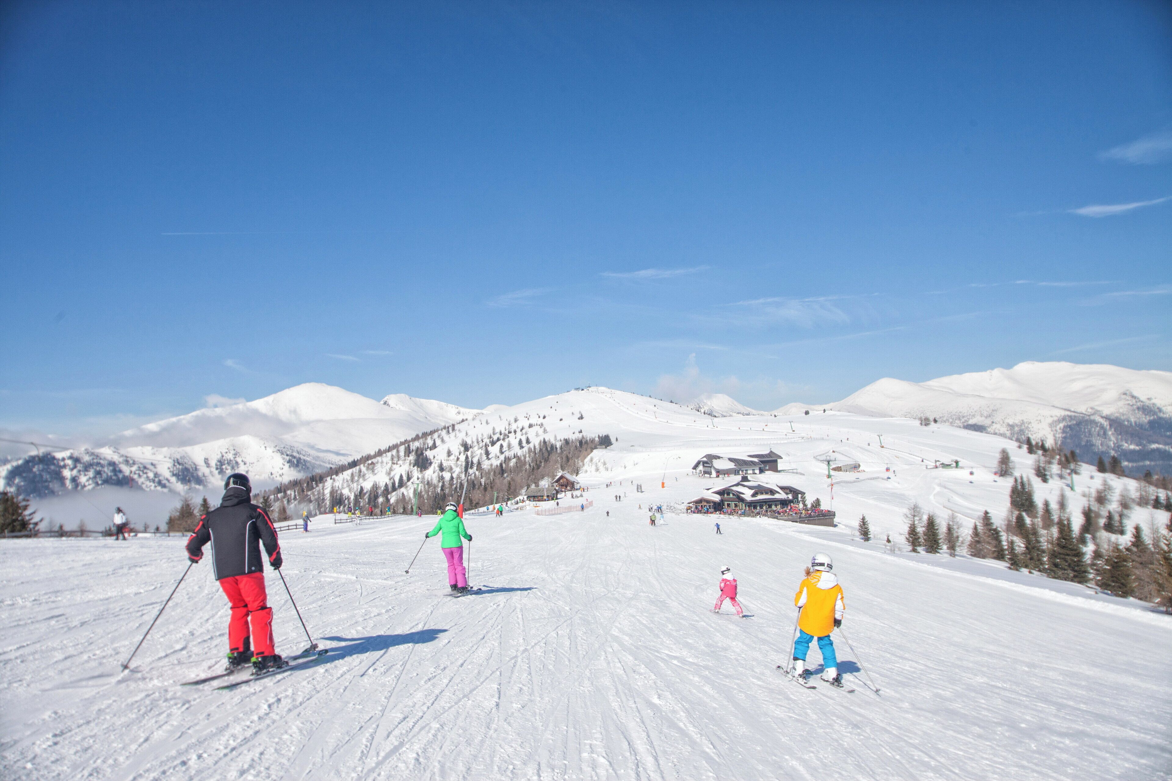 Une piste de ski avec des skieurs et un enfant, le tout entouré de montagnes enneigées et sous un ciel dégag é.