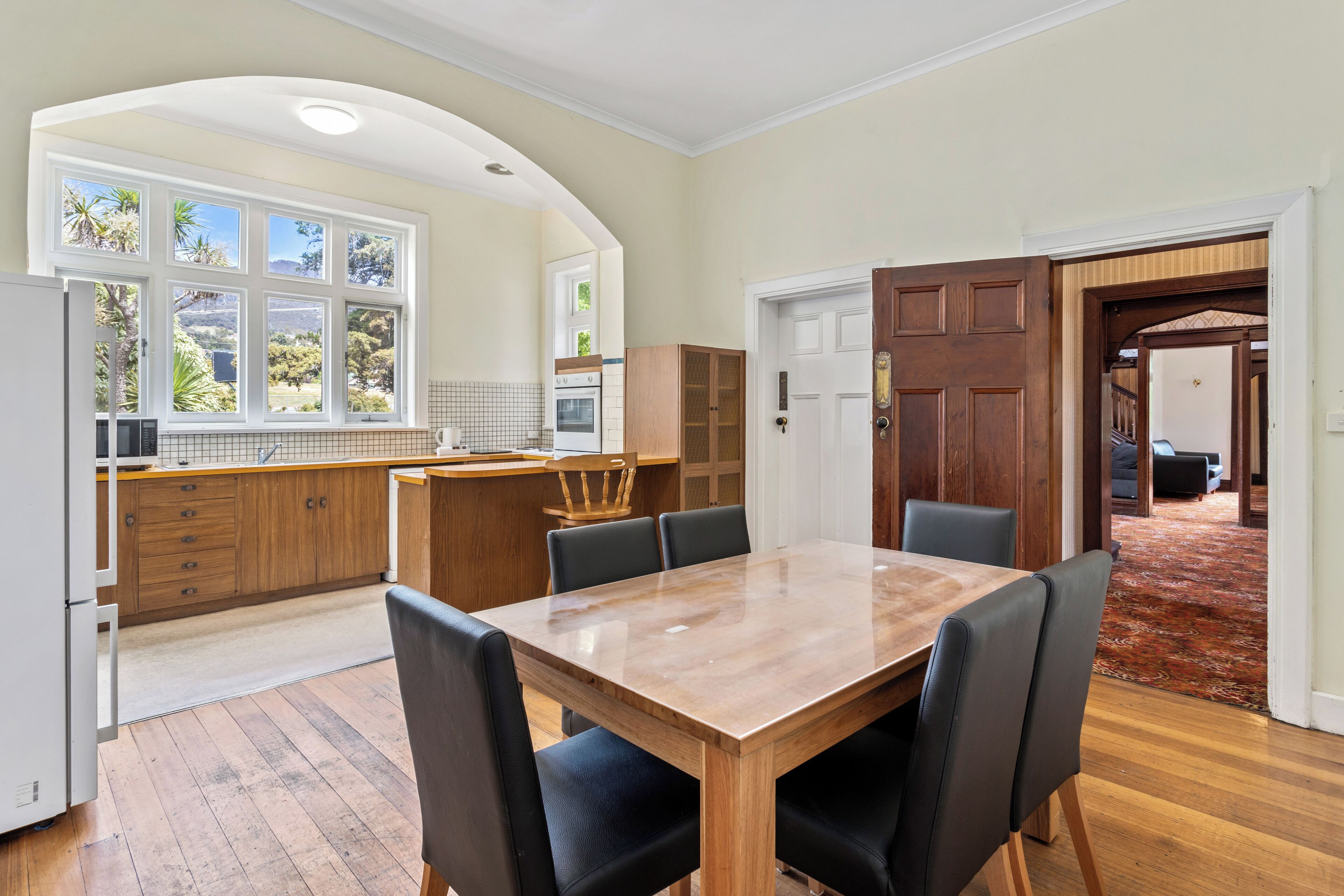 A spacious kitchen with a wooden table and chairs, a large window with a view, and an open door leading to another room.