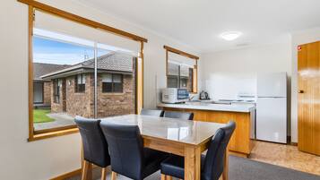 A modern kitchen with a dining area, large windows, and a view of a brick house.