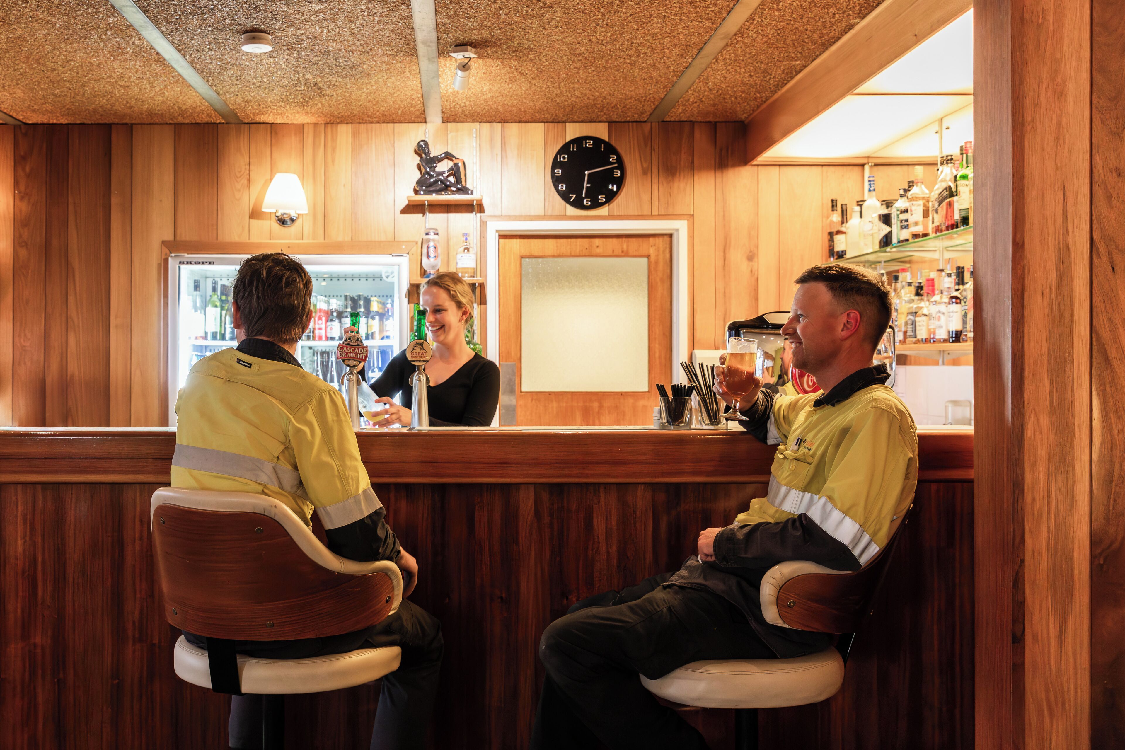 Een bar met houten lambrisering, een klok en planken met flessen.