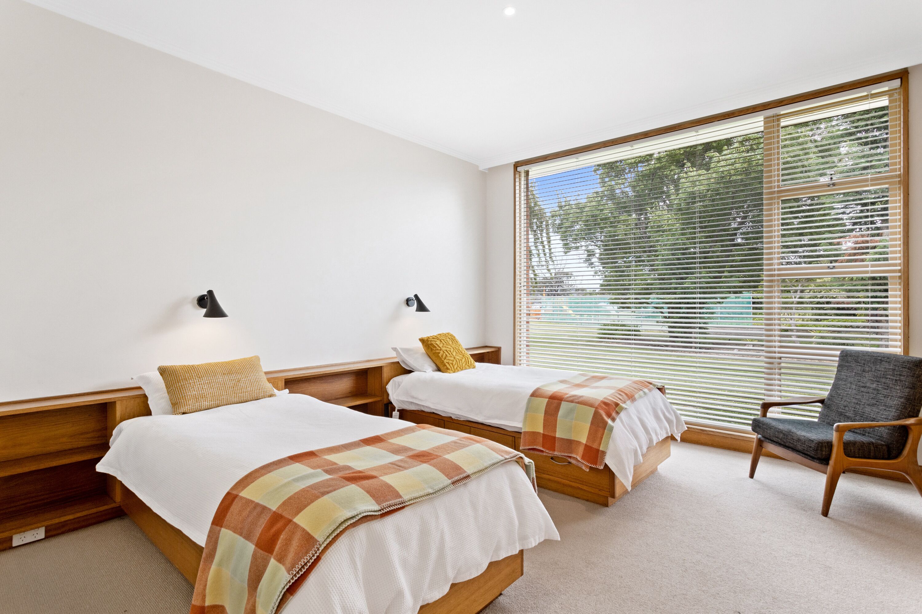 Quarto de hotel com duas camas, uma cadeira e janelas amplas com persianas.