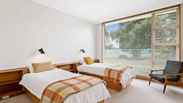 Quarto de hotel com duas camas, uma cadeira e janelas amplas com persianas.