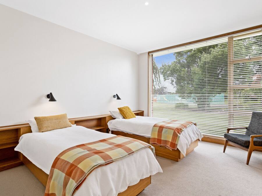 Quarto de hotel com duas camas, uma cadeira e janelas amplas com persianas.