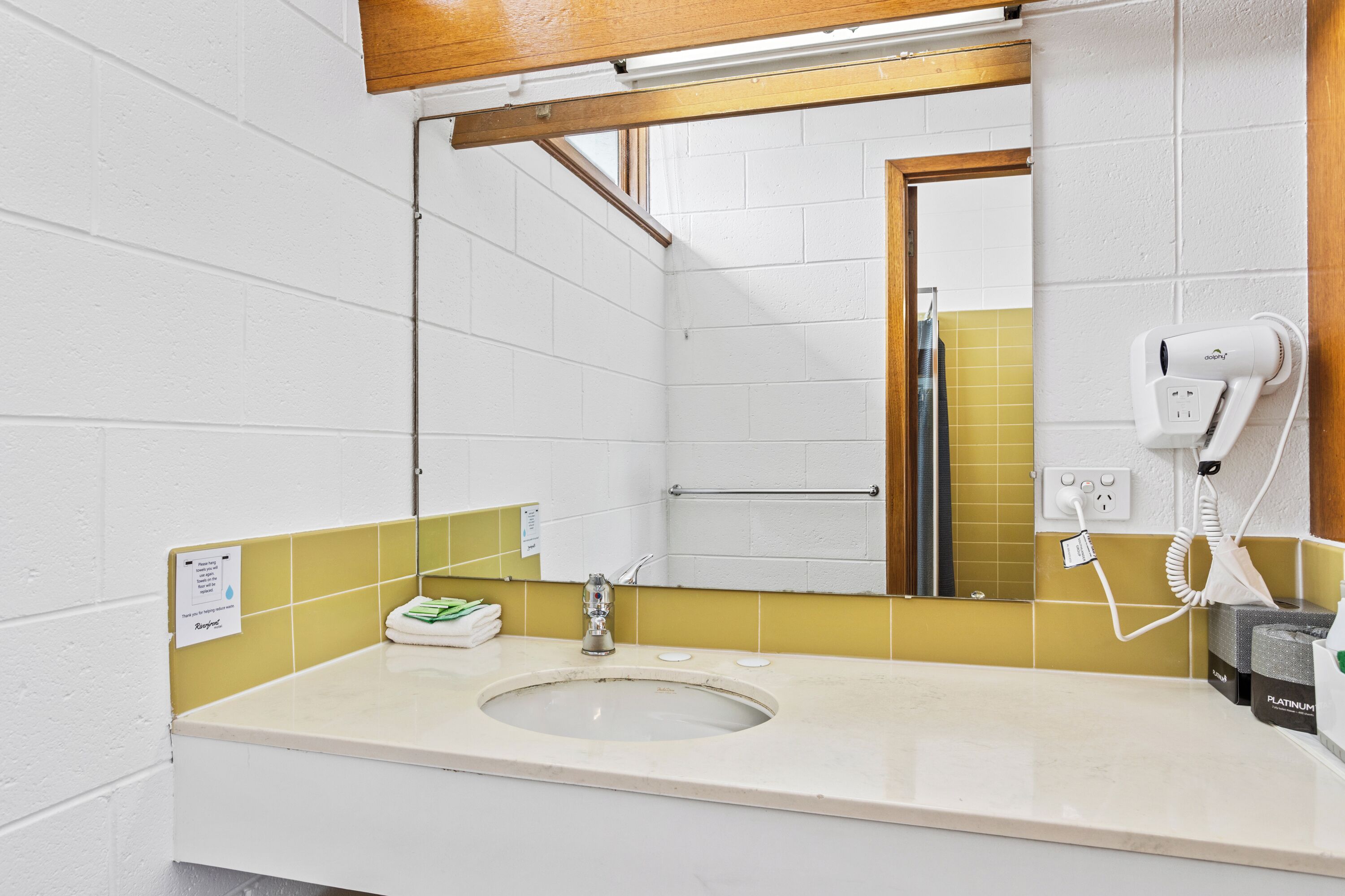 Une salle de bain équipée d’un lavabo, d’un miroir, d’un distributeur de serviettes et d’un sèche-cheveux fixé au mur.