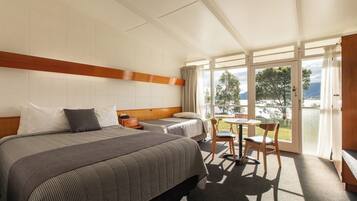 Une chambre d’hôtel avec deux lits, une petite table, des chaises et une vue sur l’extérieur grâce à une grande fenêtre.