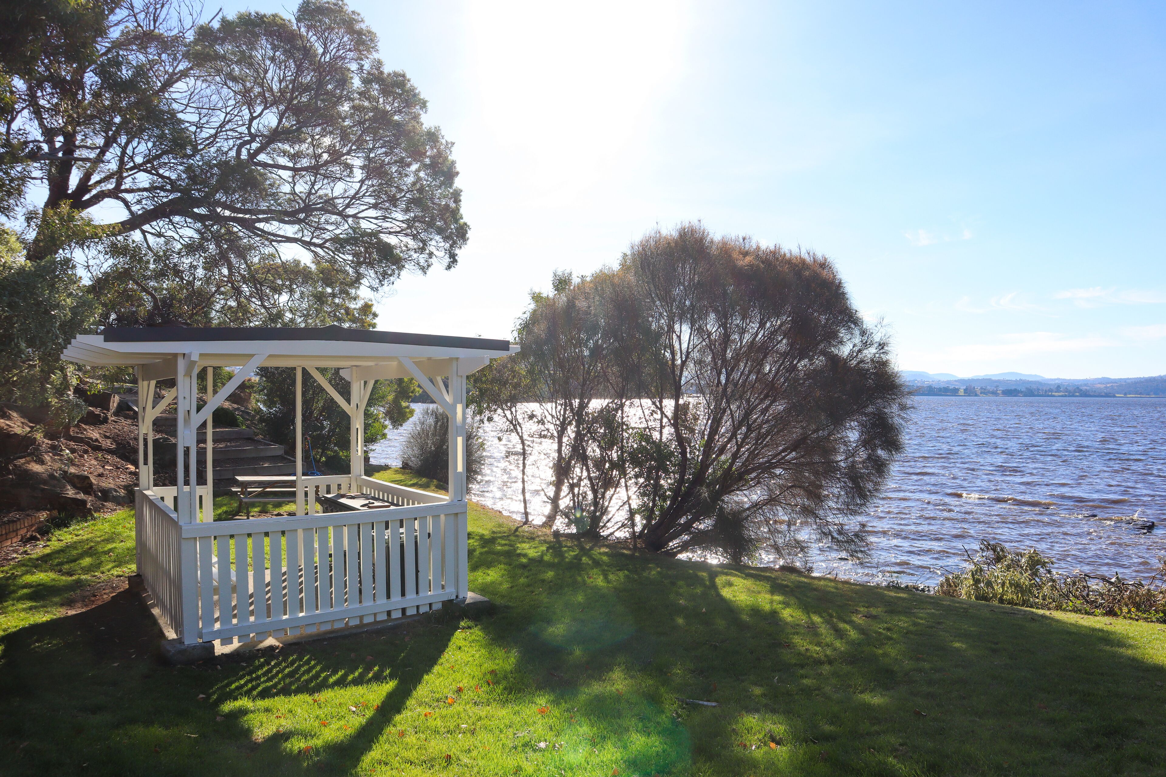 A gazebo with a white railing, a picnic table, and a grassy area beside a lake.