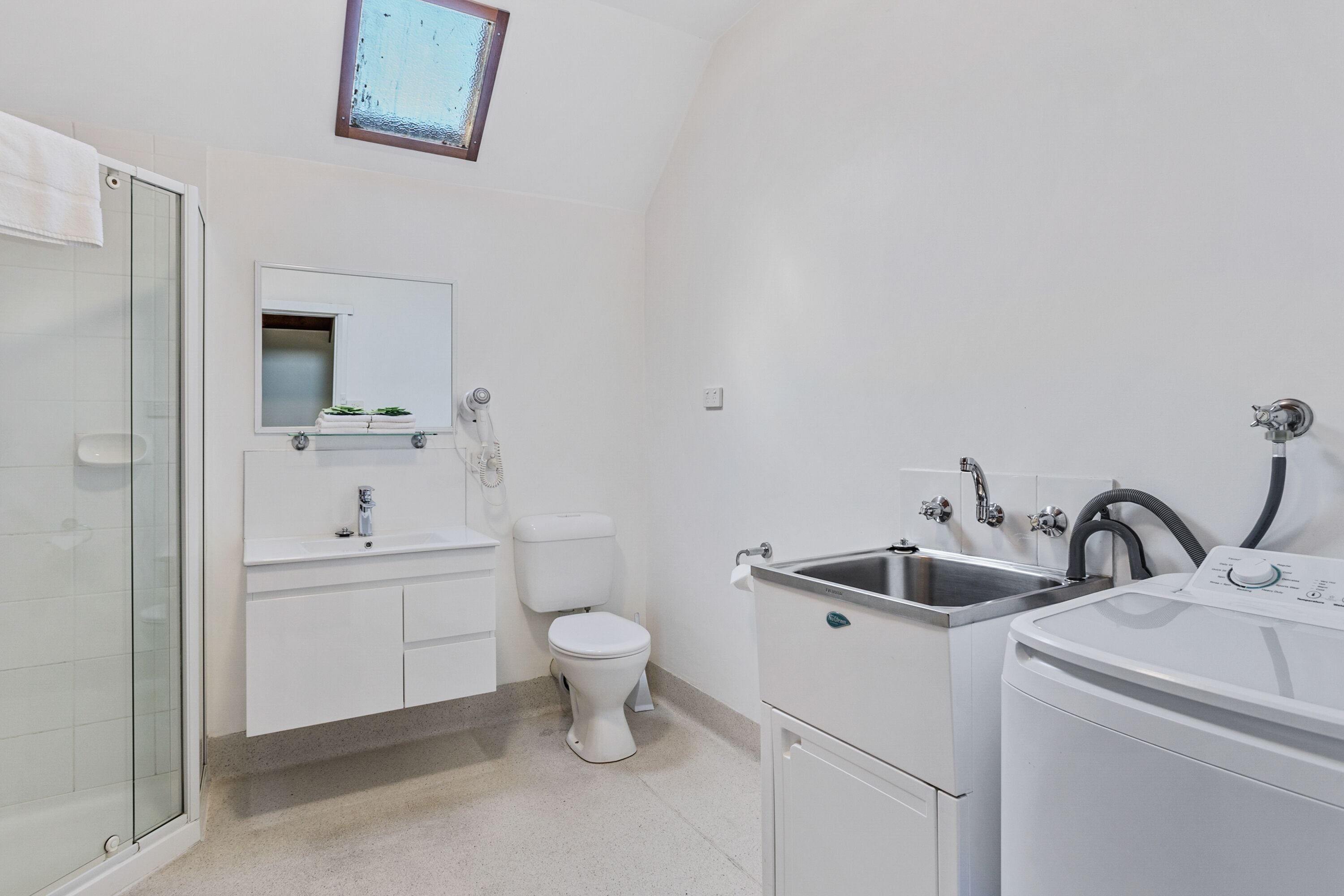 A modern bathroom with a glass shower enclosure, a white toilet, a sink with a mirror, and a washing machine.