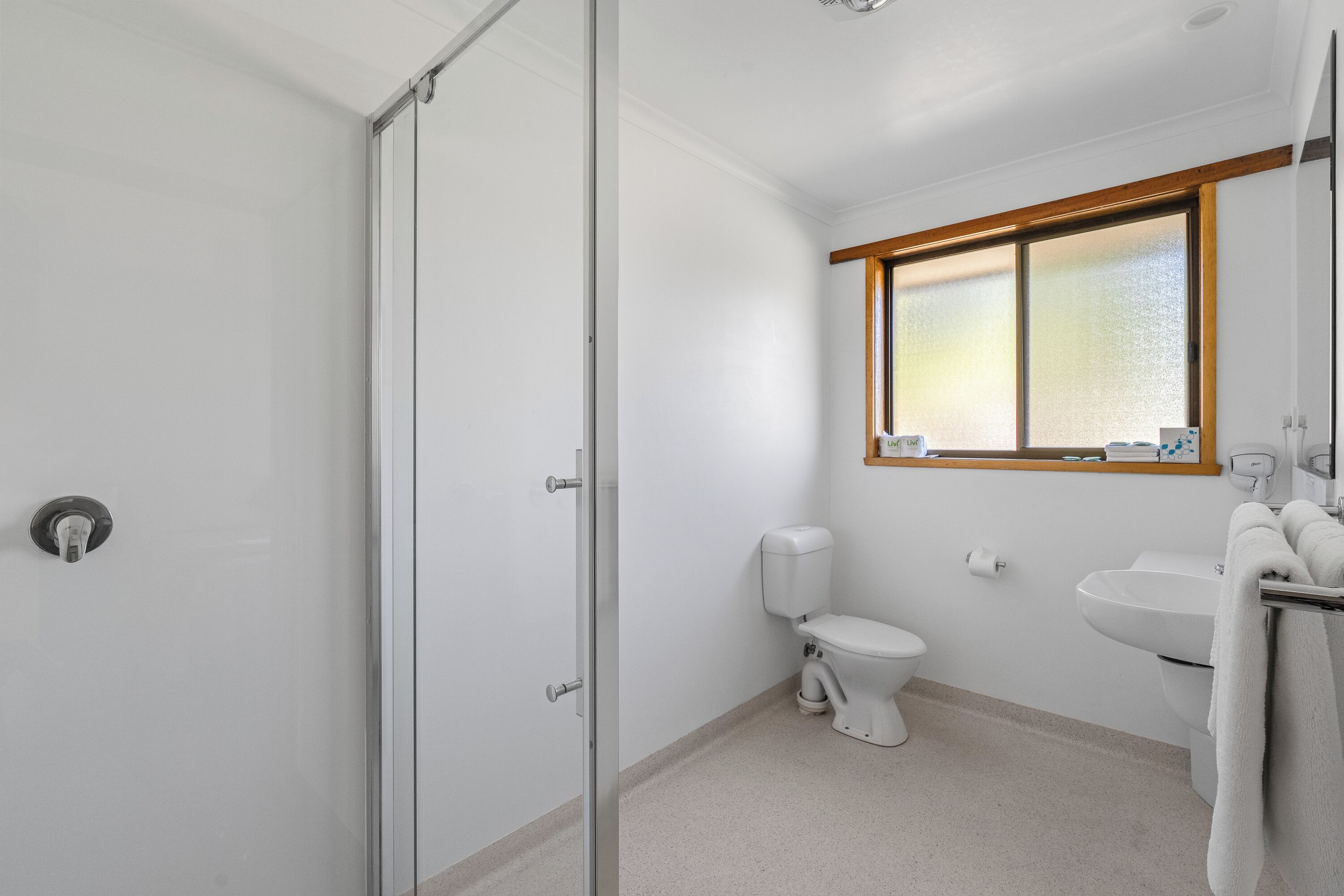 A bathroom with a glass shower door, a toilet, a sink, and a window.
