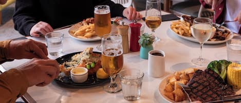 A dining table with plates of food, glasses of beer, and a steak.