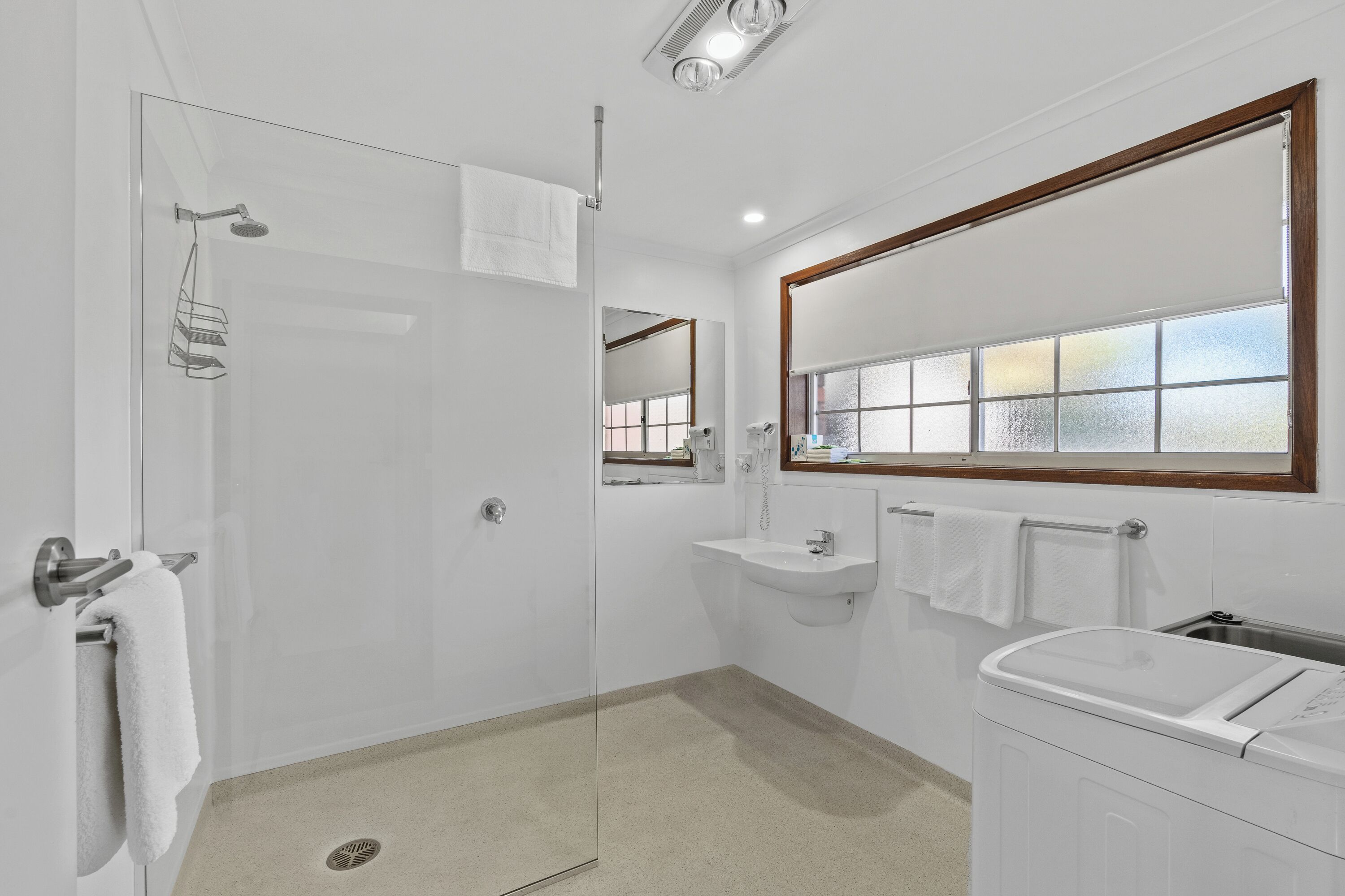Un baño moderno con cabina de ducha de vidrio, lavamanos con tocador y ventana con cristal satinado.