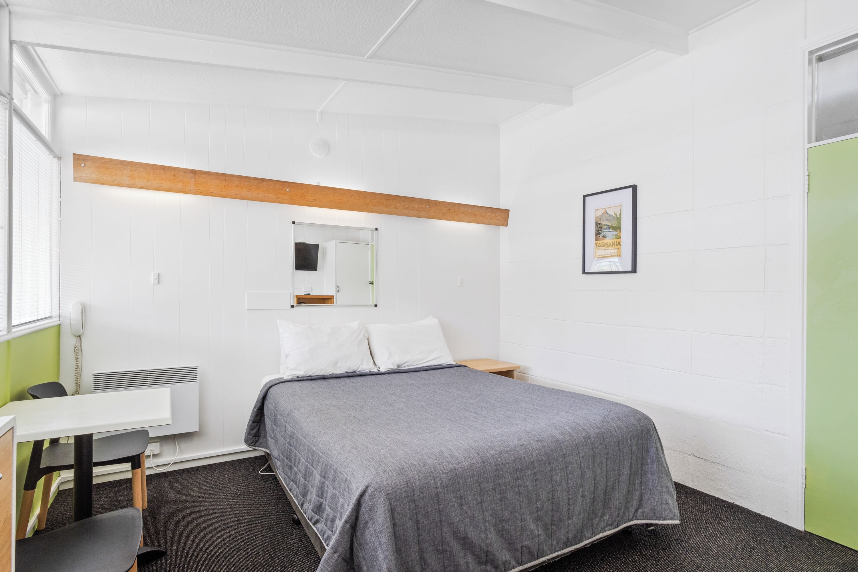 A single-bed room with a desk, a mirror, a framed picture on the wall, and a radiator.